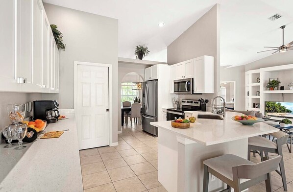 A modern kitchen with white cabinetry, a central island, and a dining area with a view of the outdoors. - Scarlett - Fantastic Rental with 2 King Size Beds (Cape Coral)