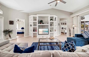 A living room with a sofa, coffee table, and a TV. There are bookshelves and a ceiling fan. - Scarlett - Fantastic Rental with 2 King Size Beds (Cape Coral)