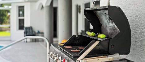 Una parrilla al aire libre con hamburguesas y mazorcas de maíz asándose, cerca de una piscina.