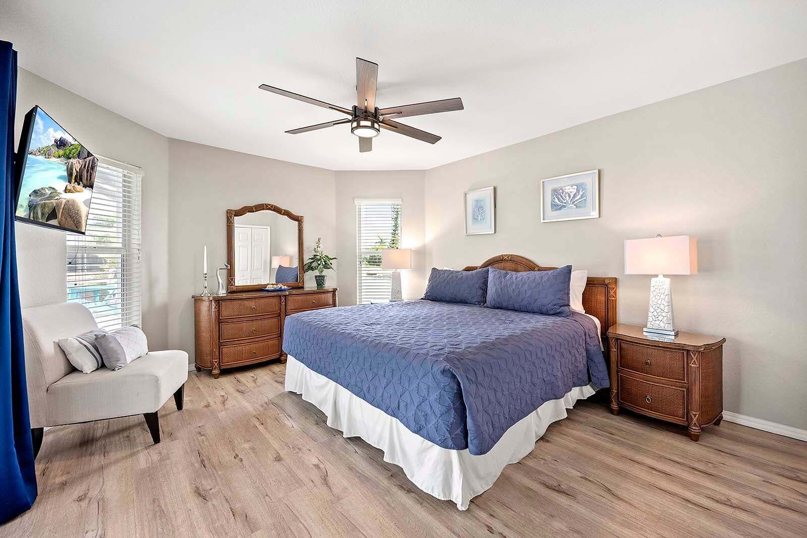 A bedroom with a bed, a dresser, a nightstand, a ceiling fan, and a window with blinds.