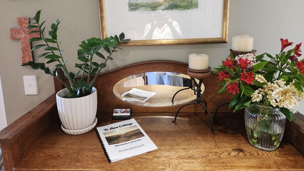 A wooden bench with a framed painting, a potted plant, a candle, and a booklet titled "Te Ava Cottage". -  Farm stay-Tranquil & quiet, relaxation country style (Sentry Hill)