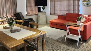 A living room with a wooden dining table, a red sofa, and a television on a stand. -  Farm stay-Tranquil & quiet, relaxation country style (Sentry Hill)