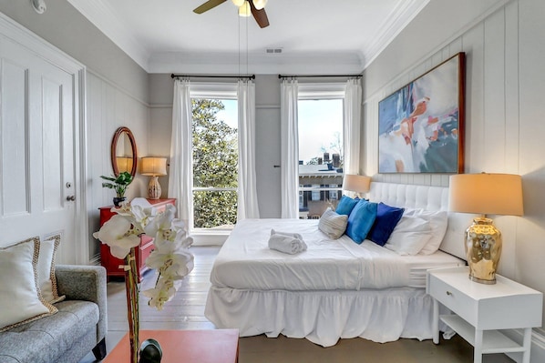 A hotel room with a large bed, two bedside tables, a chair, a ceiling fan, and a window with curtains.