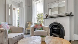 Un salón con chimenea, dos sillones, una mesa redonda de madera y una planta en maceta.