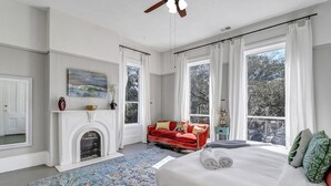 Un dormitorio amplio con una cama grande, un sofá rojo, una chimenea y ventanas grandes con vistas a árboles.