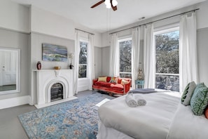 Un dormitorio amplio con una cama grande, un sofá rojo, una chimenea y ventanas grandes con vistas a árboles.