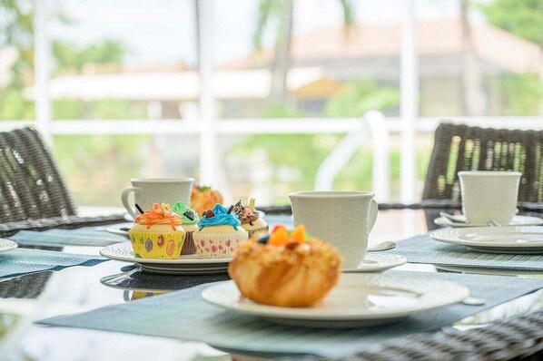 Una mesa con platos blancos, una taza blanca y un cupcake amarillo con glaseado colorido.