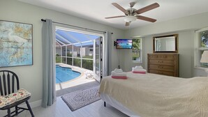 Une chambre dotée d’un grand lit, d’un ventilateur de plafond, d’une télévision, d’une commode en bois et donnant sur une piscine extérieure.