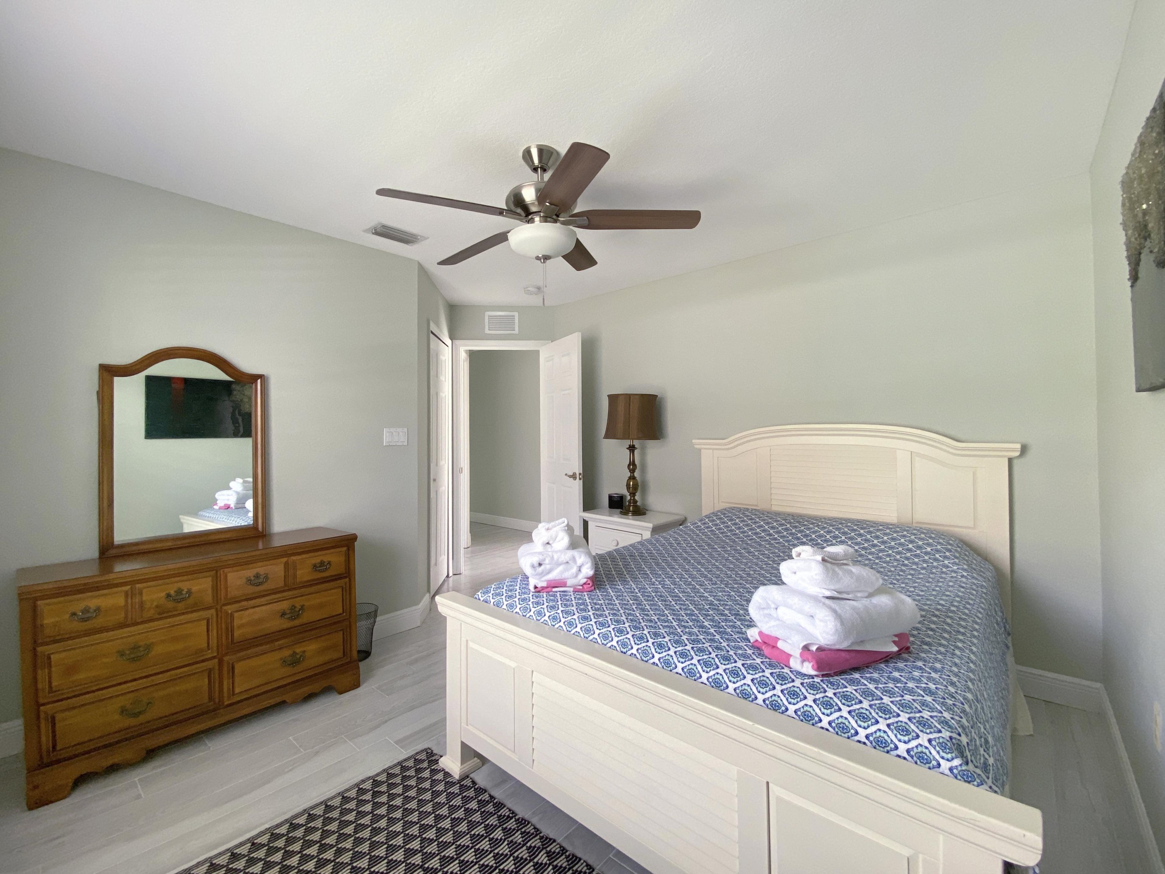 Een slaapkamer met een bed, een dressoir, een plafondventilator en een spiegel.