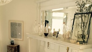 A room with a white fireplace mantel, a beige sofa with patterned cushions, a wooden stool, and a large mirror above the mantel. - Beautiful Clinton Hill House (Brooklyn)