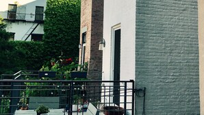 An outdoor patio with a table and benches, surrounded by a white wall and a brick building. - Beautiful Clinton Hill House (Brooklyn)