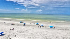 Una playa con cielos despejados, aguas tranquilas y varias sombrillas azules.