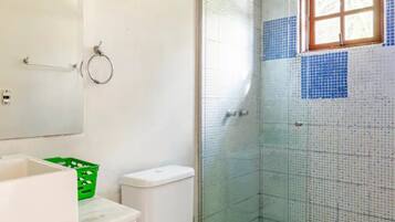 A bathroom with a toilet, a green trash bin, a white sink, and a glass-enclosed shower area.