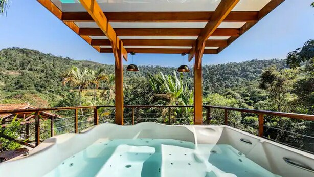 A hot tub with a wooden pergola overhead, surrounded by lush greenery and hills. - Wonderful farmhouse in Bragança, a refuge close to São Paulo. (Chácaras Fernão Dias)
