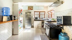 A modern kitchen with a refrigerator, microwave, stove, and gas stove. There is a water dispenser and a gas cylinder. - Wonderful farmhouse in Bragança, a refuge close to São Paulo. (Chácaras Fernão Dias)