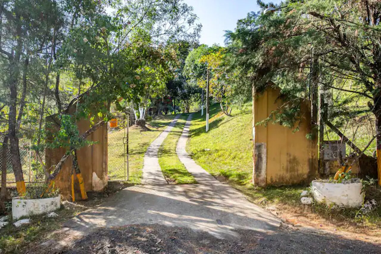 A pathway leading through a fenced area with trees and a yellow building in the background.