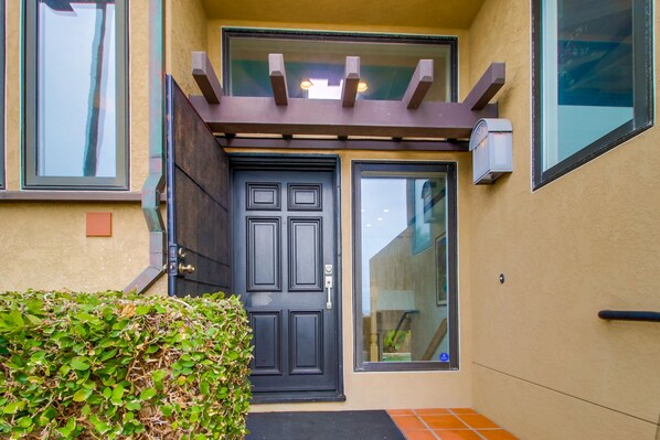 A black door with a small window above it, a small porch area with a bench, and a tiled entrance.