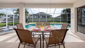 A dining area with a table set for four, overlooking a swimming pool. - Casa Pura Vida pool home with three bedrooms plus (Cape Coral)