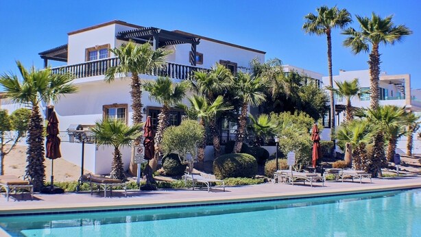 A modern hotel with a pool, palm trees, and a clear blue sky.
