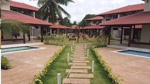 A resort with a central pathway leading to multiple buildings with red-tiled roofs, surrounded by pools and greenery. - Beachfront apartment on Itamaracá Island/PE - Itaoca Residence Condominium (Ilha de Itamaracá)