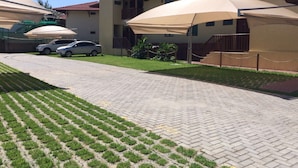 A building with a paved driveway, parked cars, and outdoor umbrellas. - Beachfront apartment on Itamaracá Island/PE - Itaoca Residence Condominium (Ilha de Itamaracá)