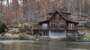 Une cabane dotée d’un balcon, d’une terrasse et offrant une vue sur un lac entouré d’arbres.