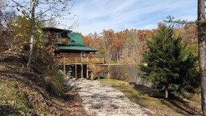 Une cabane avec un quai s’avançant dans un lac, entourée d’un paysage automnal.