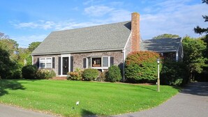 A two-story house with a brick chimney, a front porch, and a well-maintained lawn. - Walk to town, baseball games, Oyster Pond (Chatham)