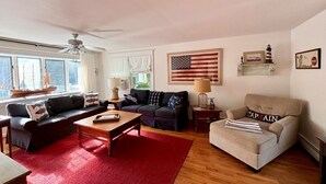 A living room with a red rug, two sofas, a coffee table, and a ceiling fan. - Walk to town, baseball games, Oyster Pond (Chatham)