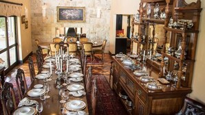 Un comedor formal con una larga mesa dispuesta para una comida, rodeada de sillas de madera y una pared de piedra.
