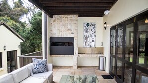 Un patio exterior con una chimenea de piedra, una mesa de centro de vidrio y un sofá blanco con cojines estampados.