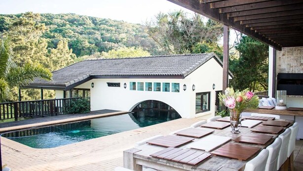 Un área junto a la piscina con mesa, sillas blancas y un florero.