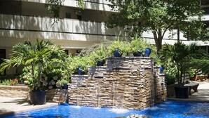 Une piscine agrémentée d’une cascade en pierre, entourée de plantes en pot et d’arbres.
