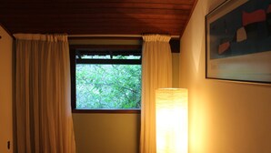 Een kamer met een raam, gordijnen, een lamp en een lijst met een afbeelding aan de muur.