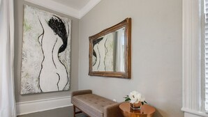 Une pièce comprenant un grand tableau abstrait, un miroir, un banc et une petite table sur laquelle est posé un vase.