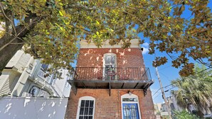 Un bâtiment à deux étages, construit en briques, doté d’un balcon, d’une porte bleue et d’une fenêtre.