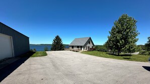 A residential driveway leading to a house with a dock, surrounded by trees and a body of water.