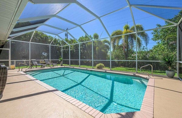 A swimming pool with a glass enclosure, surrounded by lounge chairs and potted plants.