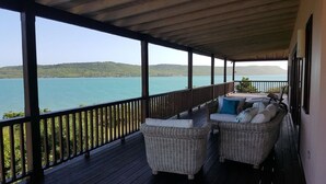Un espace extérieur abrité, aménagé avec des meubles en osier et offrant une vue sur un lac et des collines.