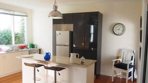 Cozinha moderna com ilha central, banquetas, geladeira e um relógio na parede.