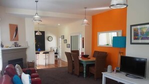 Uma sala de estar com um sofá vermelho, uma área de refeições com mesa e cadeiras, uma televisão em um suporte e uma lareira.