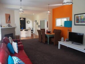 Een woonkamer met een rode bank, een eethoek met een tafel en stoelen, een televisie op een dressoir en een open haard.