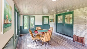 A room with a wooden ceiling, green doors, a dining table with chairs, and a brick wall.