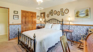 A bedroom with a four-poster bed, a wooden door, a ceiling fan, and a wall with framed pictures.