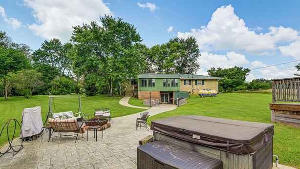 A backyard with a patio, outdoor furniture, a hot tub, and a house with a green roof.