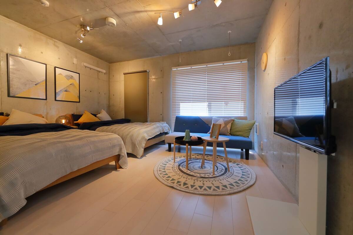 A modern bedroom with two beds, a sofa, a TV, and artwork on the walls.