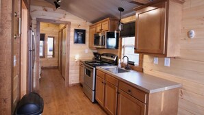 A compact kitchen with wooden cabinets, a stainless steel refrigerator, a microwave, an oven, and a sink.