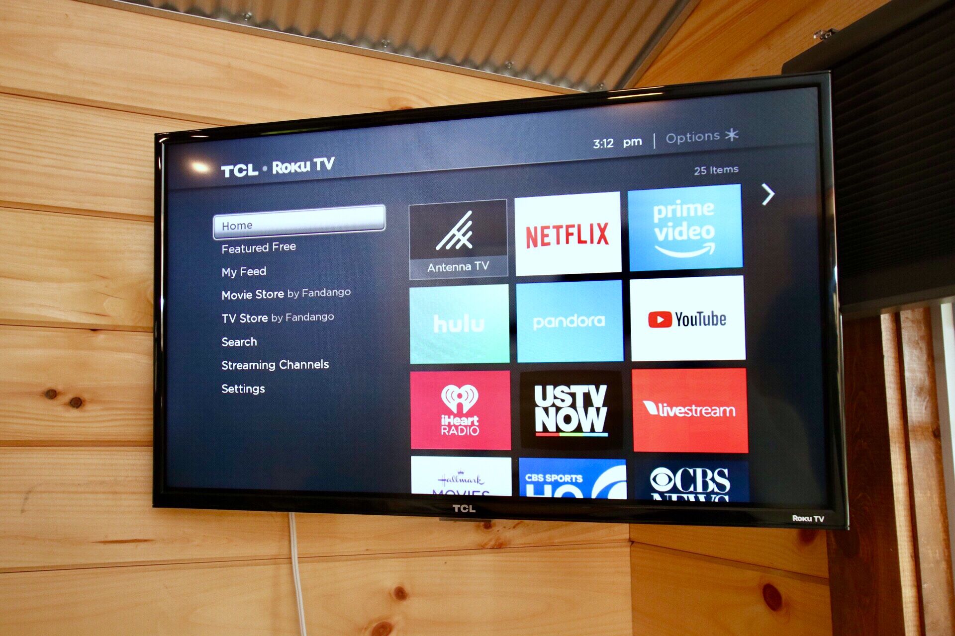 A TCL Roku TV mounted on a wooden wall displaying various streaming service icons.