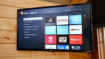 A TCL Roku TV mounted on a wooden wall displaying various streaming service icons.