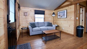 A cozy cabin interior with a sofa, a small table, a lamp, and a framed picture on the wall.